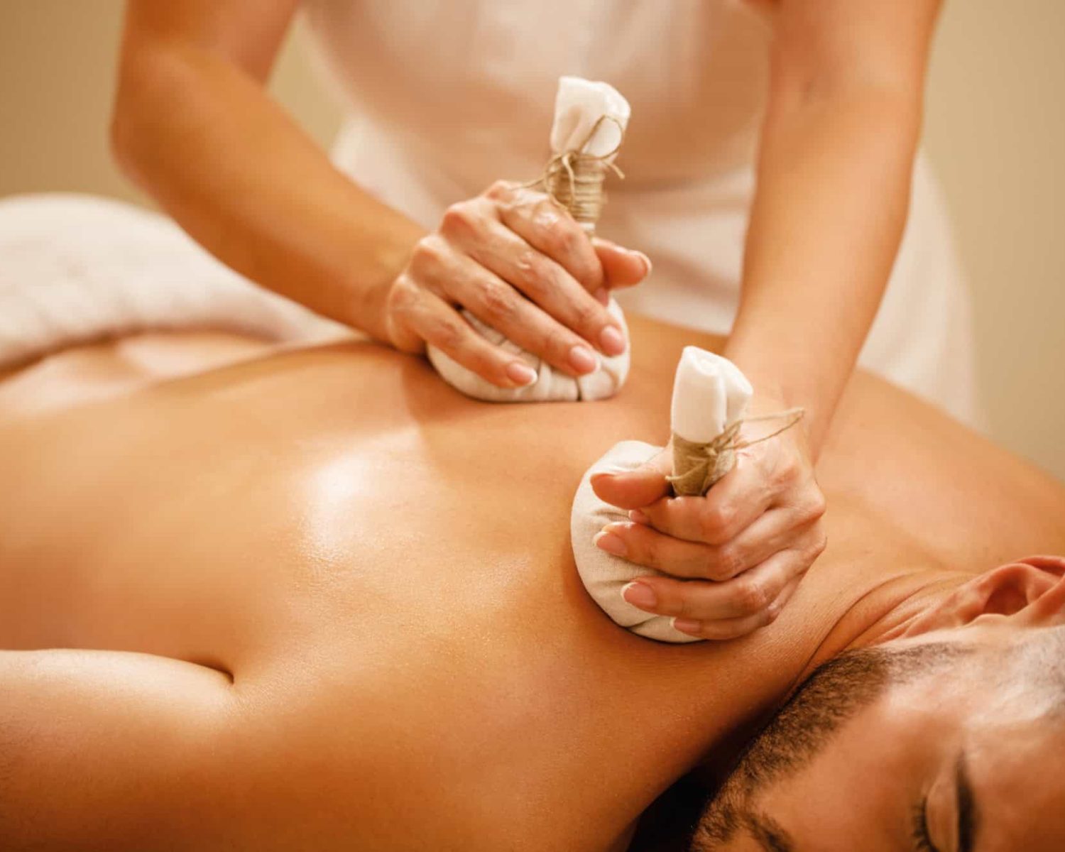 Close-up of man getting back massage with detox herbal balls at health spa.